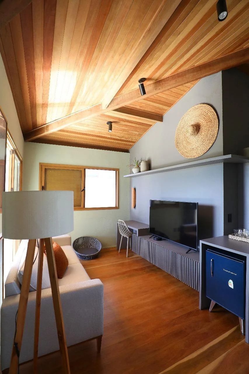 Suíte ampla com TV, luminária de piso e teto em madeira